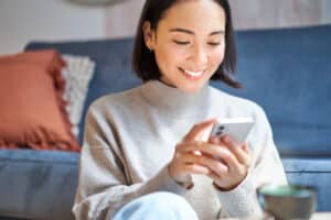 Smiling woman using her mobile phone at home, illustrating a seamless omnichannel insurance customer experience