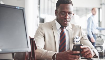 Attractive black businessman sits at the table at the car dealership, he signs a contract and buys a new car.